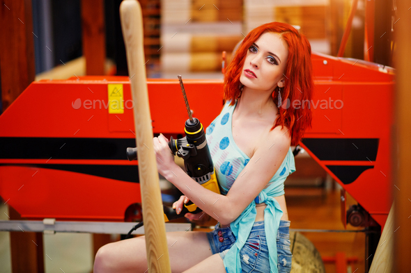 Red haired model sitting on wood sawmill with drill at store or household shop of working tools.
