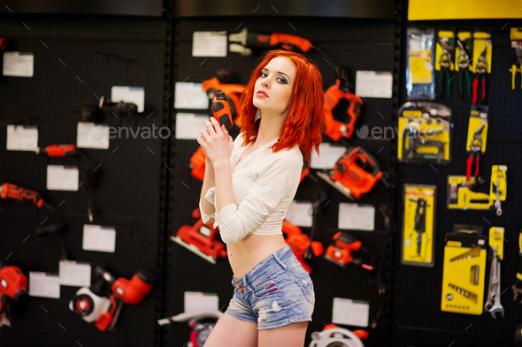 Red haired model posed with electric screwdriver at store or household shop of working tools.