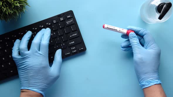 Hand in Blue Medical Gloves Holding Blood Test Tube and Typing on Keyboard alt