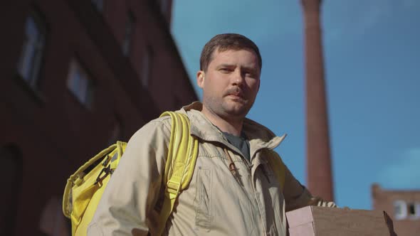 Delivery man in jacket with yellow backpack and pizza boxes standing on street