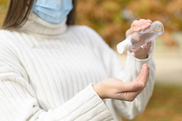 Woman with medical protection mask putting on antiseptic to disinfect her hands