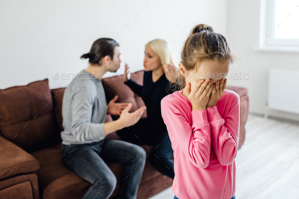 Frustrated little girl feeling depressed while angry parents fighting at home.