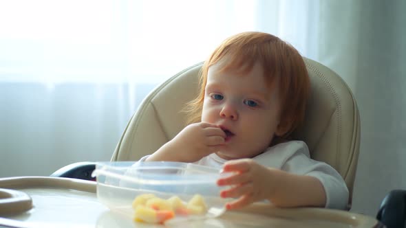 Close-up of a Baby Sitting at the Table and Eating Carrot and Other Vegetables alt