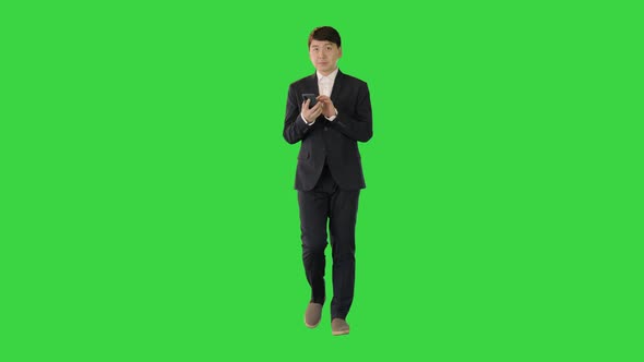 Asian Man in Suit Walks Using Mobile Phone on a Green Screen Chroma Key alt