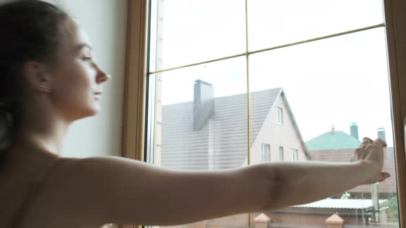 Young Attractive Girl Opening Window at Home to Let Fresh Air in Living Room