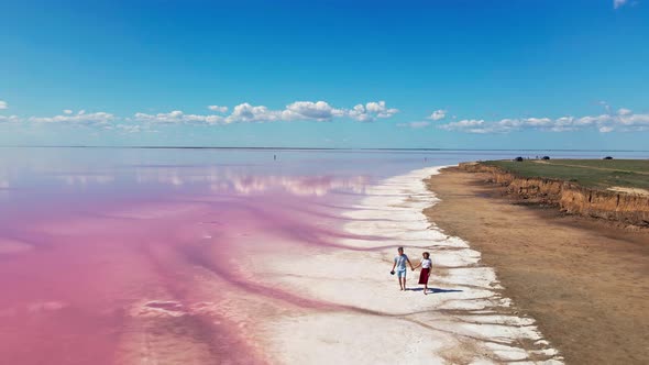 Aerial Footage of Lovely Couple Walking on Shore of Pink Mineral Lake alt