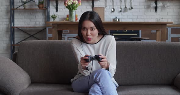 Portrait of Young Beautiful Asian Gamer Girl Sitting on Sofa and Playing in Video Games on Digital alt