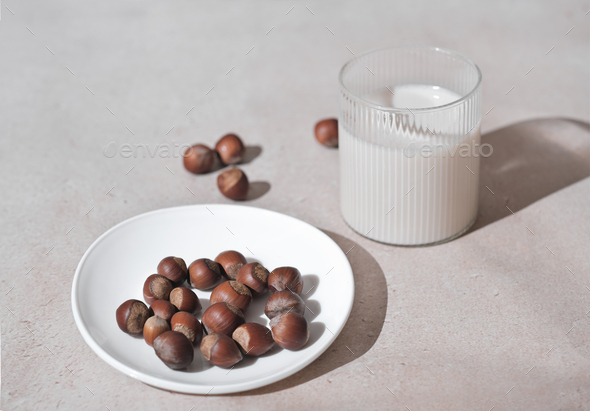 haselnut milk in a glass and nuts on a plate. alternative milk, dairy free lactose free drink.