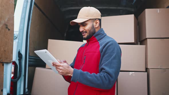 Young Courier Using Tablet in Front of the Van Full with Cardboard Boxes alt