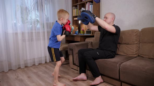 Father Boxing Coach Teaches His Son in Boxing Gloves to Hit Boxing Paws at Home alt