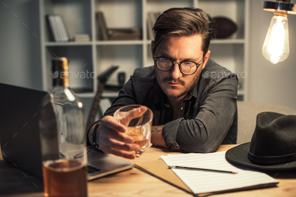 young unsuccessful musician drinking alone at workplace while trying to work on project