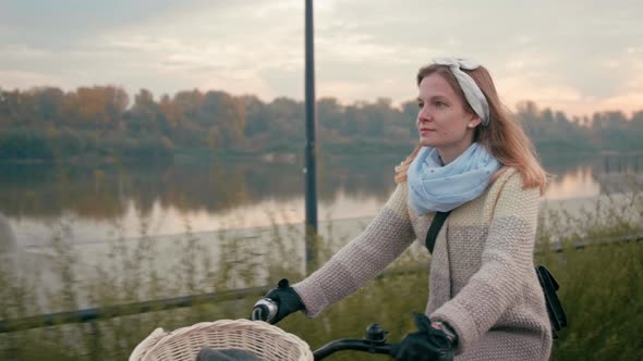 Pretty Woman Rides Bike in City in Street Near River in the Autumn Morning