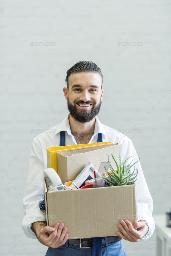 portrait of smiling businessman holding cardboard box with office supplies and quitting job
