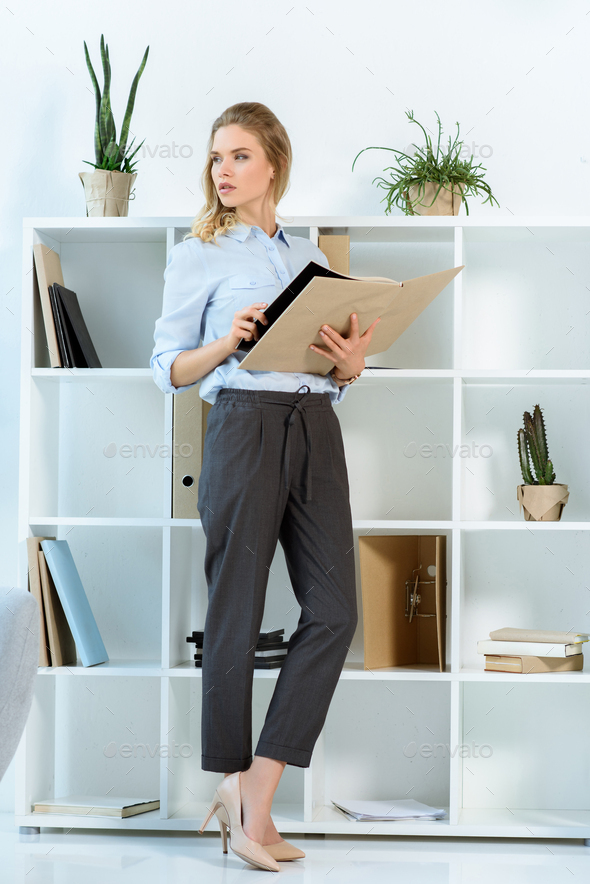 pensive businesswoman looking away while standing with work journal in office