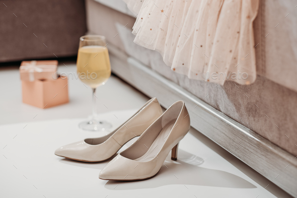 elegant beige lady shoes, vine glass and gift box next to a couch. festive tulle dress on a sofa