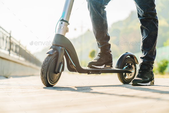 Cropped image of man in jeans and sneakers stepping on electric scooter