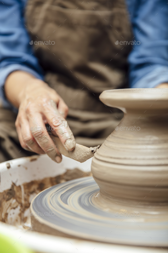 View at an senior female artist makes clay pottery on a spin wheel