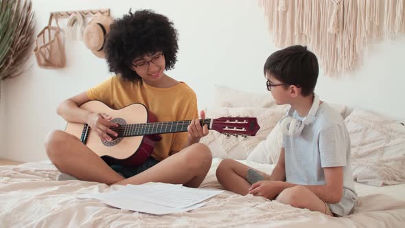 Cheerful Couple Playing Guitar While Sitting on Bed alt
