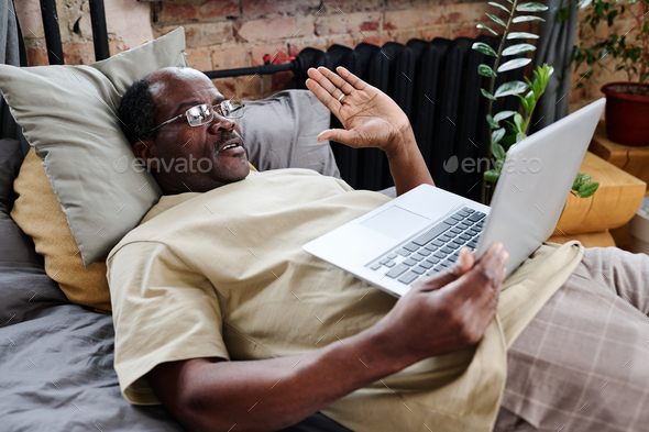 Contemporary senior black man waving hand to someone on laptop screen