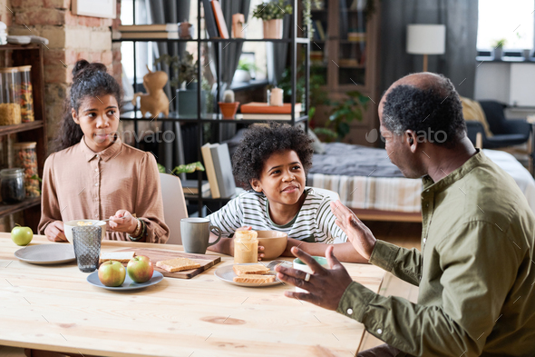 Contemporary retired black man talking to his grandchildren by breakfast
