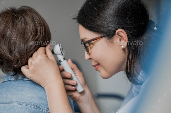 Close up of doctor examining boy\'s ear with otoscope in medical cabinet