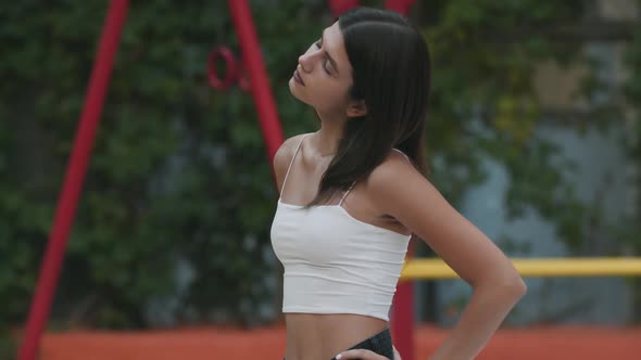 Confident Brunette Fit Woman Stretching Neck Standing on Outdoor Court alt