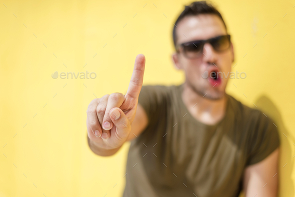 Front view of a defocus cool man saying no with sunglasses against yellow wall