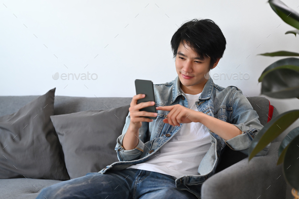 Man in using smart phone, checking social media, ordering delivery while relax on sofa.