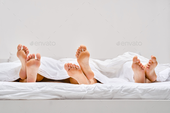 Three pairs of female soles sticking out from under the blanket