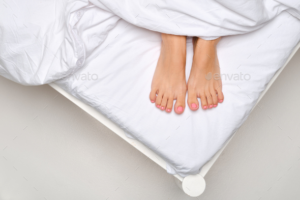 Overhead view of female soles sticking out from under the blanket