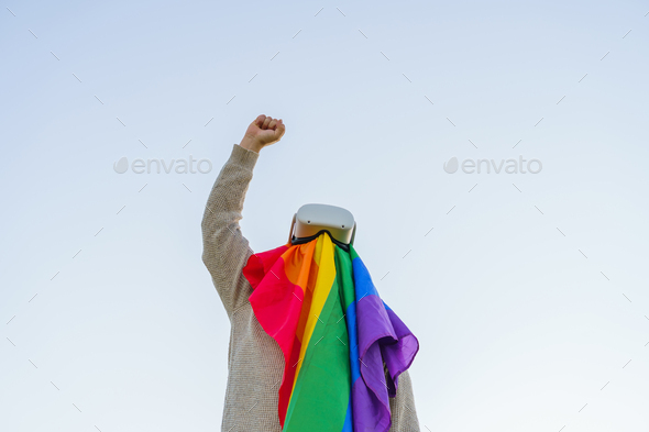 Man raising his fist in the air in protest while wearing an LGBT flag