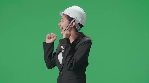 Side View Of Smiling Asian Female Engineer With Safety Helmet Dancing In The Green Screen Studio alt