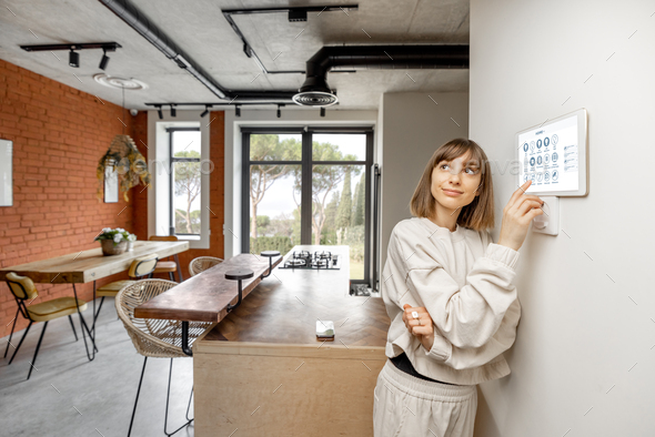 Woman controlling home devices with digital smart panel mounted on the wall