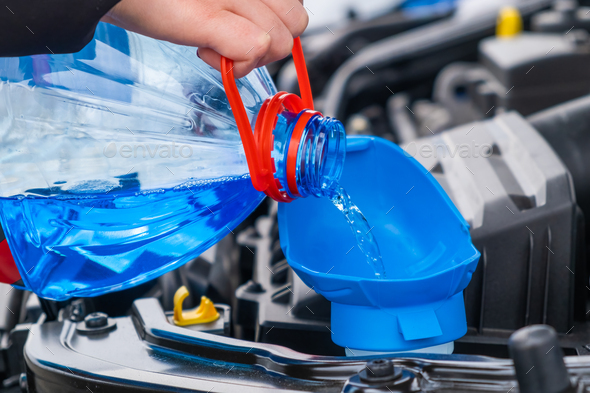 Close up driver pouring blue non freezing windshield glass washer fluid into the tank of the car