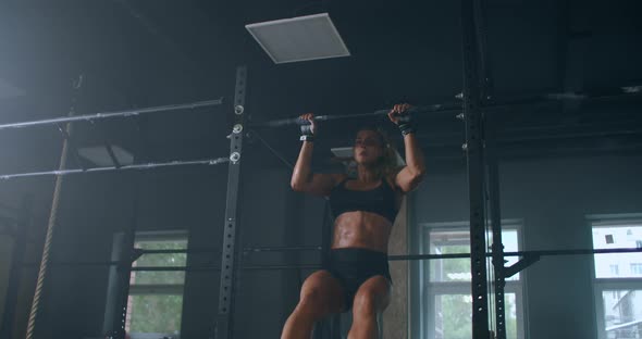 Female Athlete Swinging On Chin Up Bar. Strong Women Doing Chin-ups On Gymnastic Bars In Gym alt