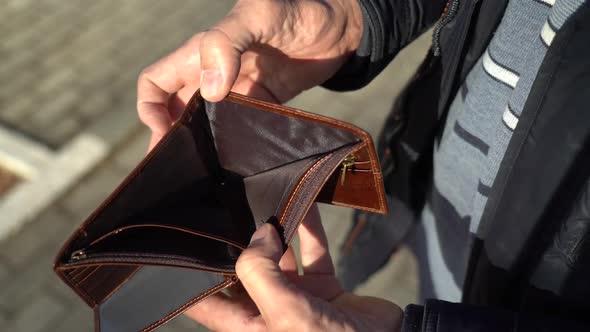 An Elderly Man Holds an Empty Purse alt