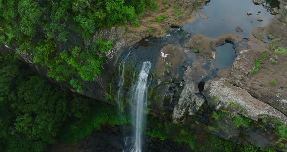 A Beautiful Woman in a White Dress on Top of a Waterfall in a Green Jungle Enjoys Her Victory alt
