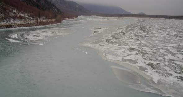 Aerial helicopter shot towards rocky, snowy Alaskan mountainside, drone footage alt