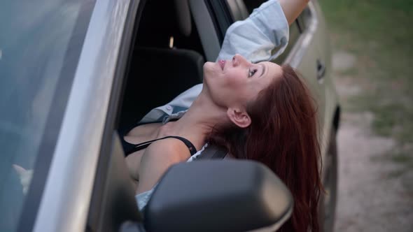Excited Carefree Young Slim Woman Leaning on Car Door Sitting on Driver's Seat Smiling Talking alt
