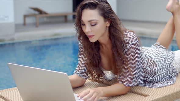 Stylish Woman with Laptop Resting on Poolside alt
