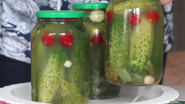 A Woman Demonstrates Jars Of Cucumbers And Tomatoes. You Can See The Process Of Fermentation Of Vege