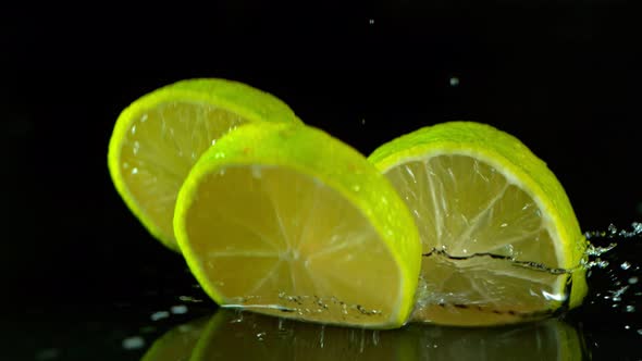 Super Slow Motion Shot of Fresh Lime Slices Falling Into Water Isolated on Black at 1000 Fps alt