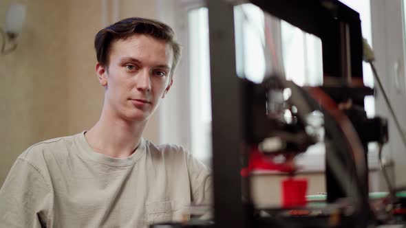 Young Man Sitting Near Working 3D Printer
