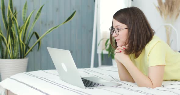 Young Beautiful Woman is Lying on the Bed in Front of a Laptop alt