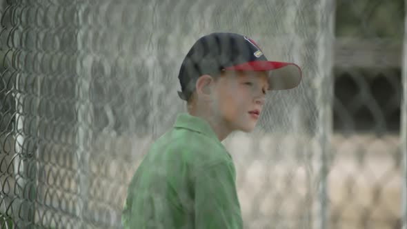 Slow motion rack focus of boy sitting in dugout behind chain link fence. alt