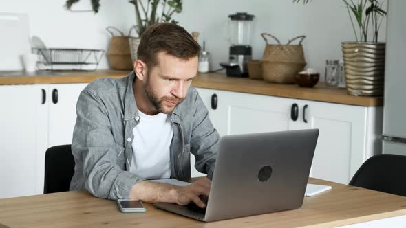 A Young Freelance Man Works At A Computer, Looks at The Monitor Screen, Is in A Room At Home alt