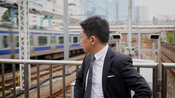 Japanese businessman waiting on a train platform alt