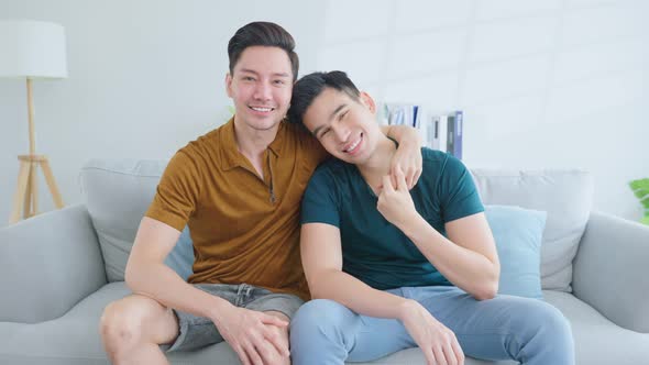 Portrait of Asian handsome man gay family sit on sofa, hugging each other and looking at camera. alt