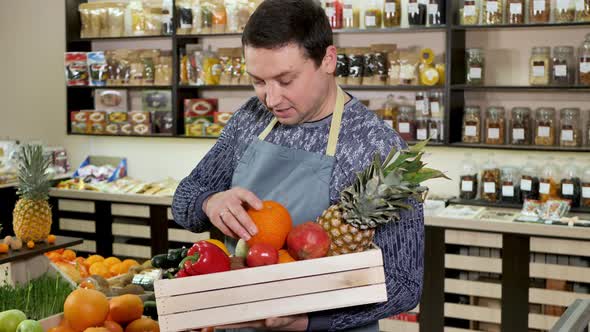 The Seller Puts the Vegetables and Fruits in a Wooden Box Looks at the Camera Smiles and Gives a