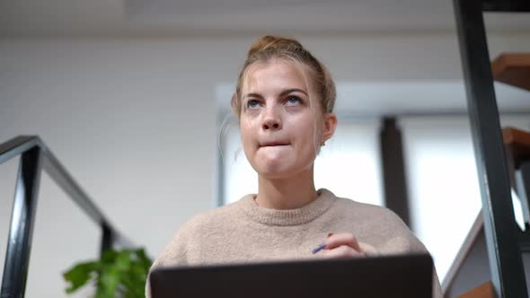 Front View Cute Teenage Girl Thinking Typing on Laptop Keyboard Sitting Indoors at Home alt